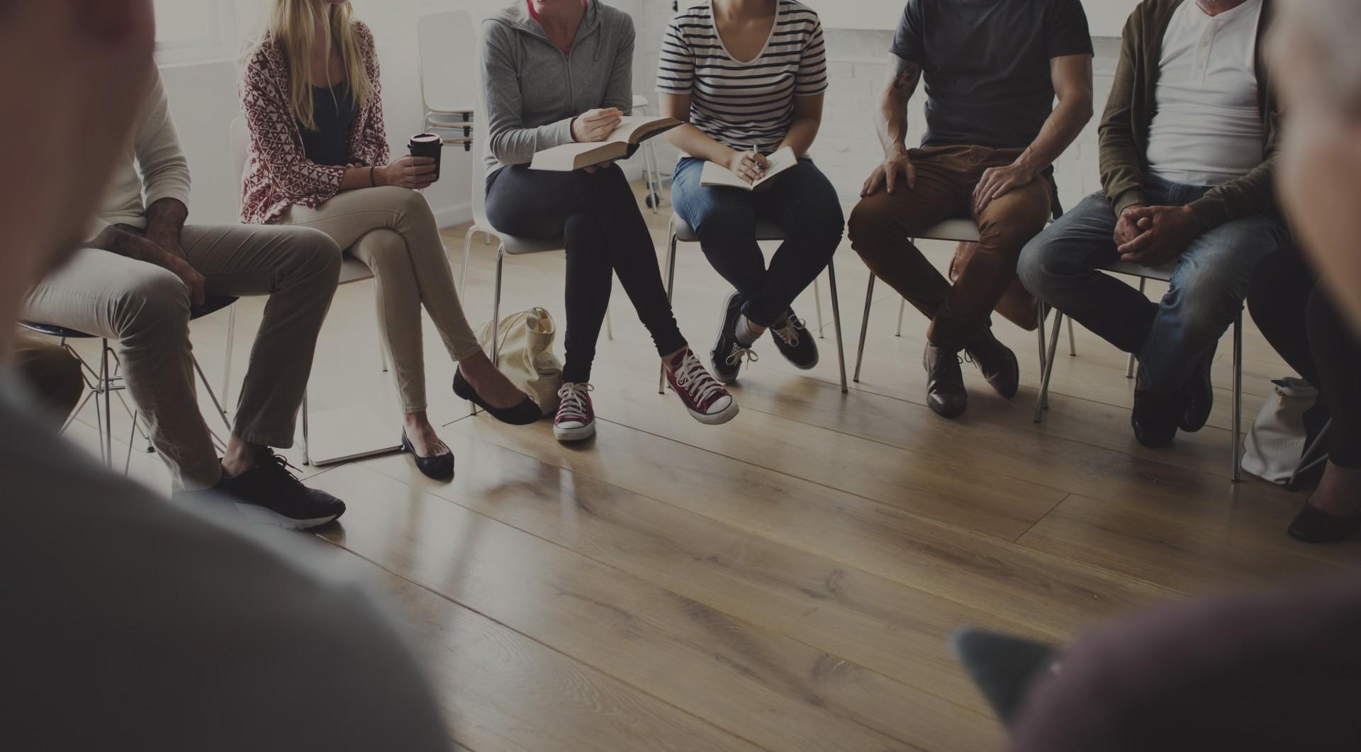 Group of people sitting on chairs in circle.