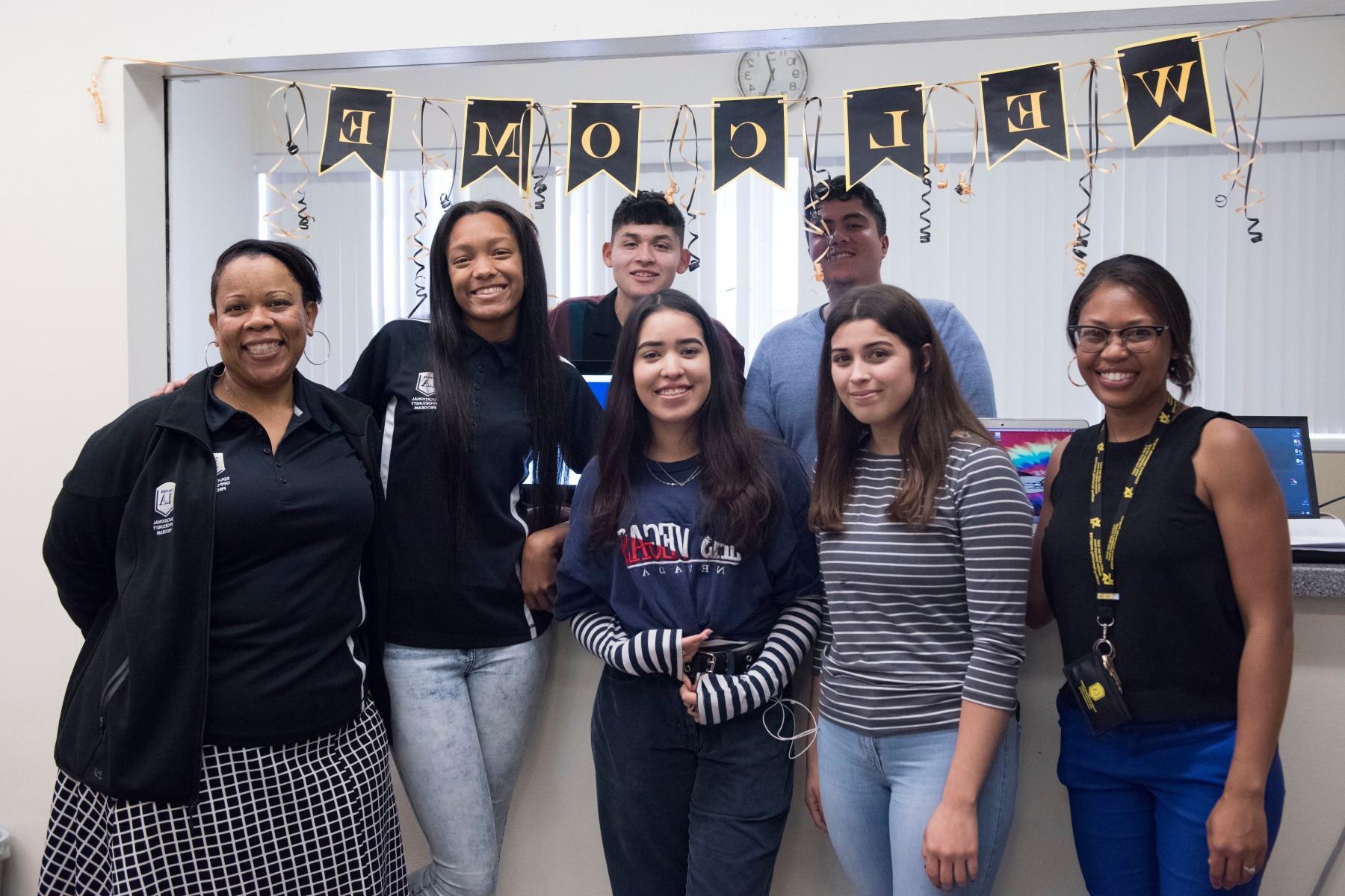 Two staff members stand with a group of five students under a welcome banner