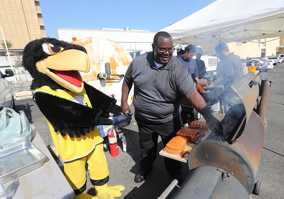 Old version of Eddie the Golden Eagle standing at a BBQ grill with a staff person.