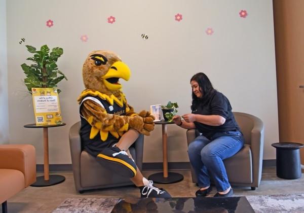 Female employee sitting on a couch next to Eddie the Golden Eagle Mascot