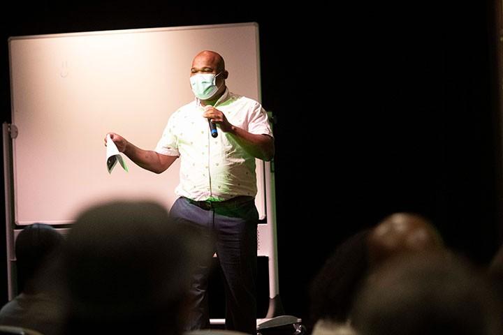 Person in mask onstage addressing audience